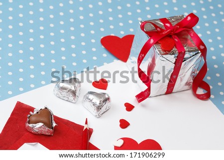 Valentine's day love message, unfinished, on white paper with pencil, hearts, gift box with valentine's day ribbon and heart-shaped chocolates isolated on blue with white dots background (polka dot)