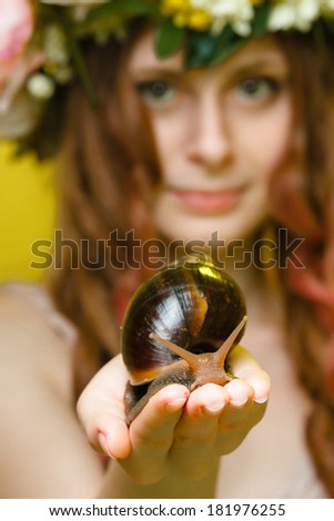 pretty girl with snail in hand and flower crown on head on yellow background