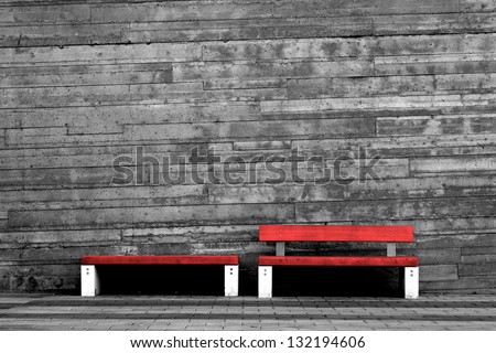 Red benches contrasted against dull concrete wall.