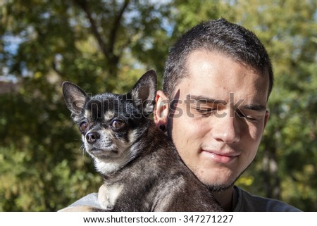Young man holding cute black chihuahua dog over green nature background