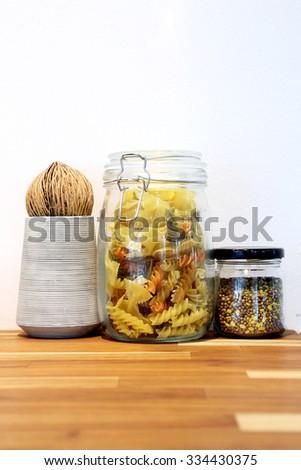 Tricolor spiral pasta and grain in glass jar on wooden table.