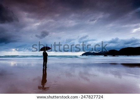 Person with umbrella under rain in the beach