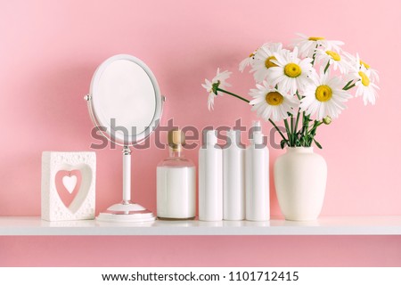 Soft pink light bathroom decor for advertising, design, cover. Cosmetic set on light dressing table. Beautiful flowers in a vase on a pink wall background, mirror on a wooden shelf. mock up