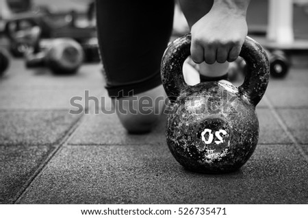 Muscular fitness woman holding old and rusty kettle bell on to the gym floor. Black and white.