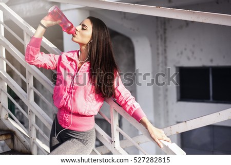 Fitness woman drinking water after jogging on metal steps