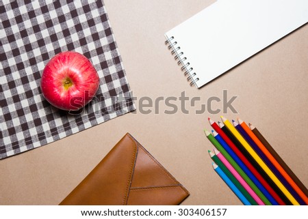 Mix of office supplies and apple on brown table striped Fabric and brown paper background