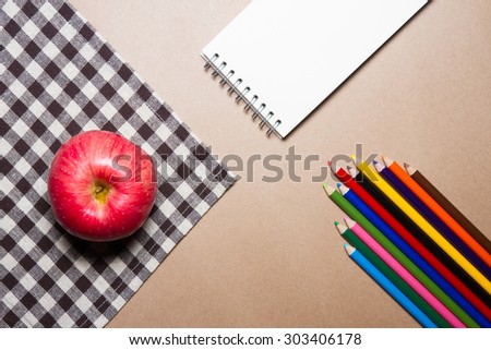 Mix of office supplies and apple on brown table striped Fabric and brown paper background