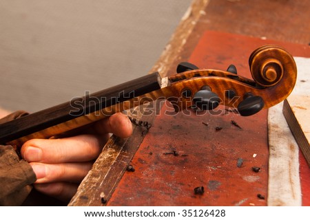 A violin maker making repairs on a violin in his shop.