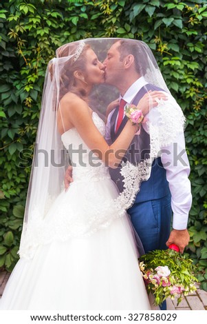 Bride and groom on wedding kissing under veil near bush