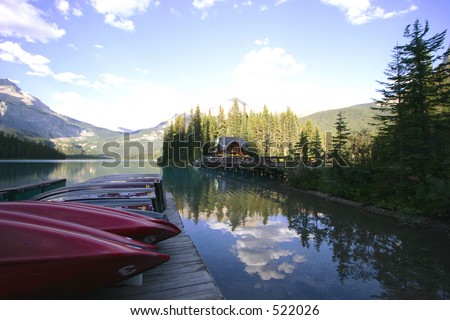 A dock of boats on a tranquil mountain lake with a small cabin in the background.