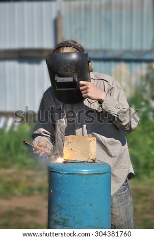 Worker welds in mask blue metal cylinder with electrode outdoor