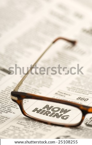 Glasses highlighting a NOW HIRING classified ad in a newspaper.