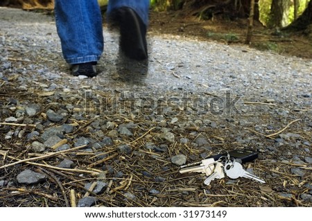 A set of house and car keys lay on the forest trail as a person walks away from them.