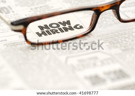 Now Hiring newspaper classified ad framed in a pair of reading glasses.