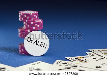 White dealer button, pink poker chips and playing cards spread out on blue felt in foreground. Copy space in upper right of image. DEALER can be removed to provide more copy space for customized text.