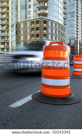 A bright orange barrel-shaped traffic pylon guides traffic along a city street.