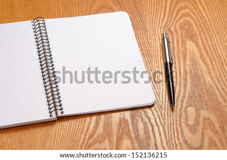 A white note book with black pen on wooden table