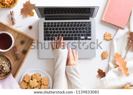 Workspace with red and yellow maple leaves, laptop, cup of tea, sweet homemade cookies. Top view of cozy office desk. Autumn background, flat lay.