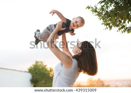 Portrait of mother and baby outdoor on the sunset. Mom and her one years old baby boy have fun on the park. Mum throws kid and child smiling and laughing
