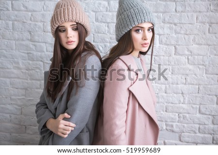 A hipster casual girls with long brown hair wearing a stylish coat and knit cap is looking aside while standing on a light white brick background on a street. Horizontal mock up.
