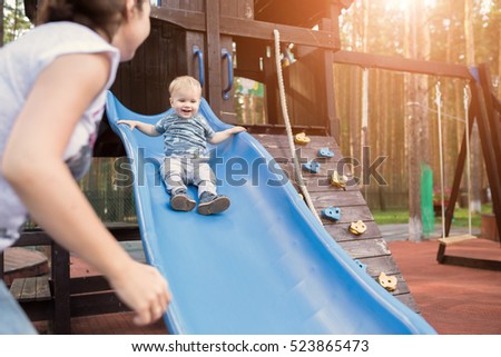 Happy young mother with her baby boy playing in colorful playground for kids. Mom with toddler having fun at summer park. Baby play in children's slide