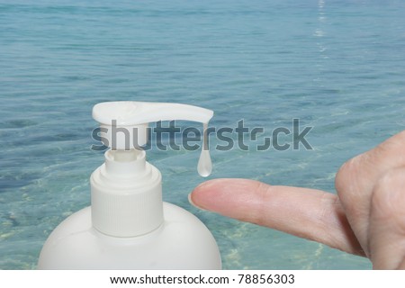 Soap dispenser with a drop of liquid soap and finger catching the drop on a sea background