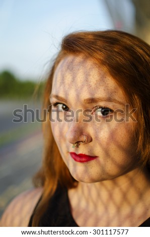 Red headed woman with nose ring with shadows on her face.