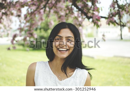 Young, South Asian woman laughing in park under an apple blossom tree