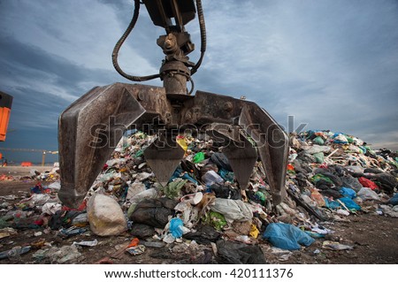Close up of mechanical arm grabbing waste from a pile at city landfill