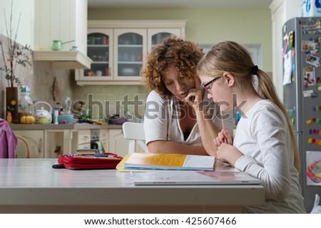 Mother helping daughter with her homework at the table in the dining room.