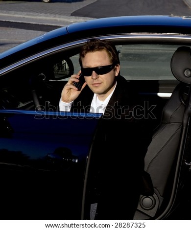 A stylish business executive in a German luxury car. He is talking on his cell phone while getting out of the car.