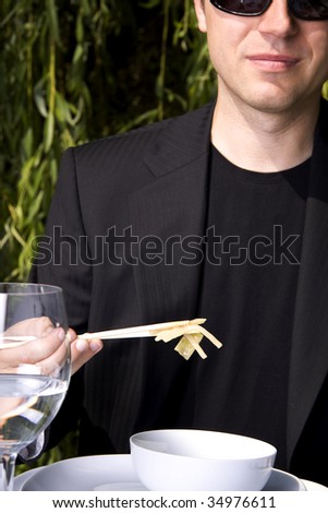 Man in a black suit is eating asian food with chop sticks
