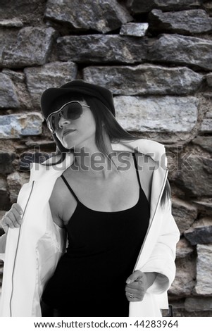 Fashion model with white jacket against a rough pattern of a historic brick wall