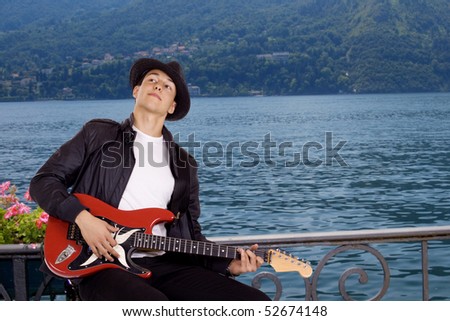 Young guitar player by the sitting at the Como lake in Italt