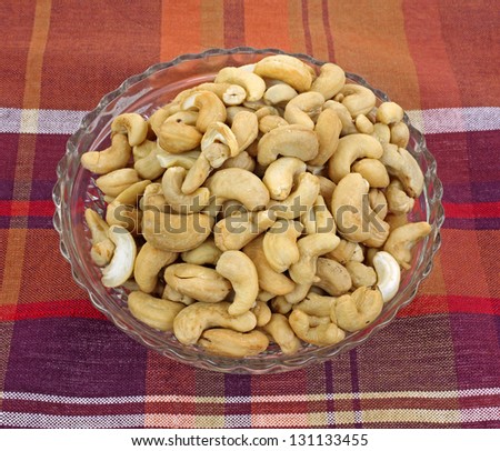 Whole unsalted cashew in a glass dish on plaid cloth.