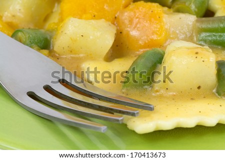 A close view of pumpkin filled ravioli, fruits and vegetables  in a butter sage sauce with fork and green plate.