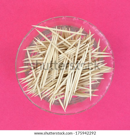 A top view of a dish full of toothpicks on a pink background.