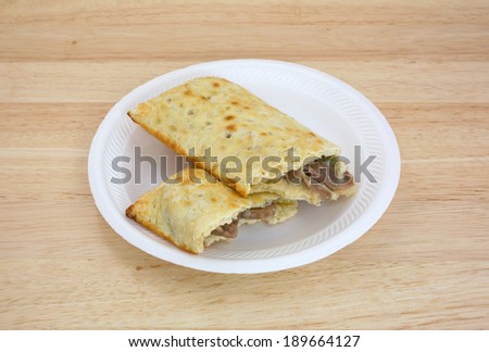 A bite of a philly steak and cheese sandwich on a white paper plate.
