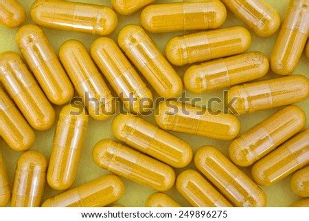 A top view of several turmeric capsules on a yellow background.