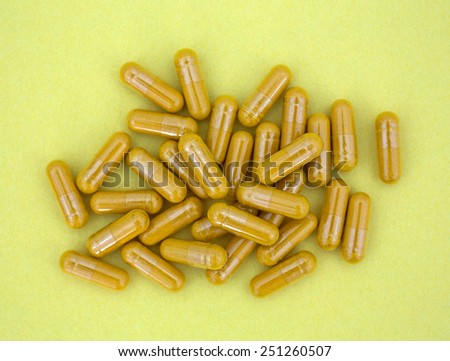 An overhead view of several turmeric capsules on a yellow background.