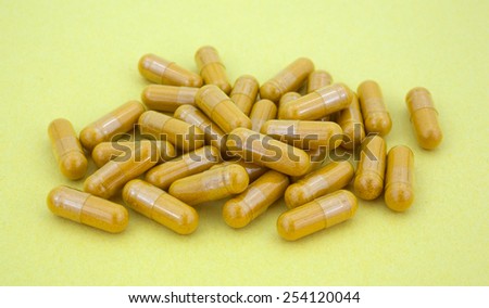 A side view of several turmeric capsules on a yellow background.