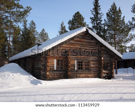 Romantic snow covered log cabin between the trees in a holiday resort in Lapland, Finland.