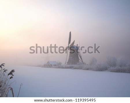 Sunrise in winter over a frozen canal and windmills at the famous dutch UNESCO site Kinderdijk, Holland.