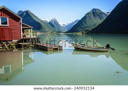 Reflection of a boat, a jetty, a red boathouse and mountains in the tranquil water of FjÃ?Â¦rlandsfjord, part of the Sognefjord in the village of FjÃ?Â¦rland or Mundal, Sogn og Fjordane, Fjord Norway.
