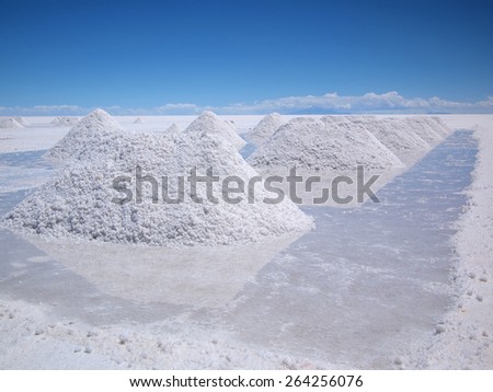 Piles of drying salt waiting for harvest and reflection in the water at the Salar de Uyuni salt flats in Bolivia.