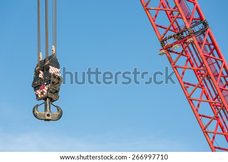 Red crane boom with steel hook against blue sky