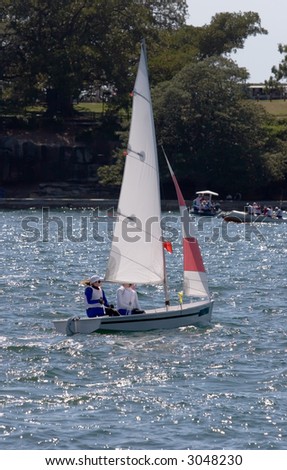 A small sail boat racing on Sydney Harbour with spectator craft in the background