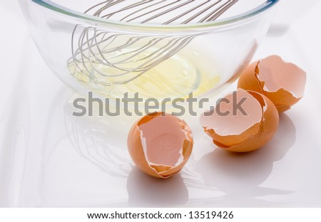 Three broken eggs and a bowl with egg white and whisk