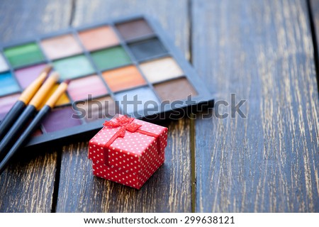 Gift box and brushes for makeup with palette on wooden table.