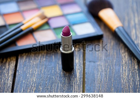 brushes for makeup with palette and lipstick on wooden table.